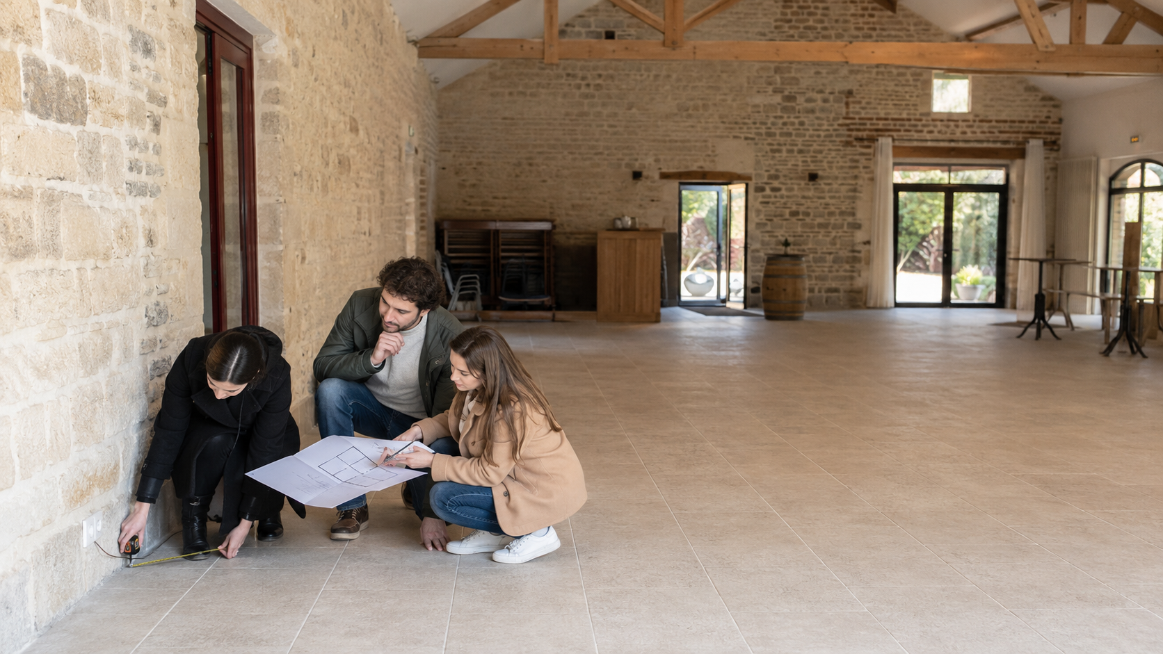 Un couple et une coordinatrice vérifient le plan et les contraintes techniques d'une salle de réception vide